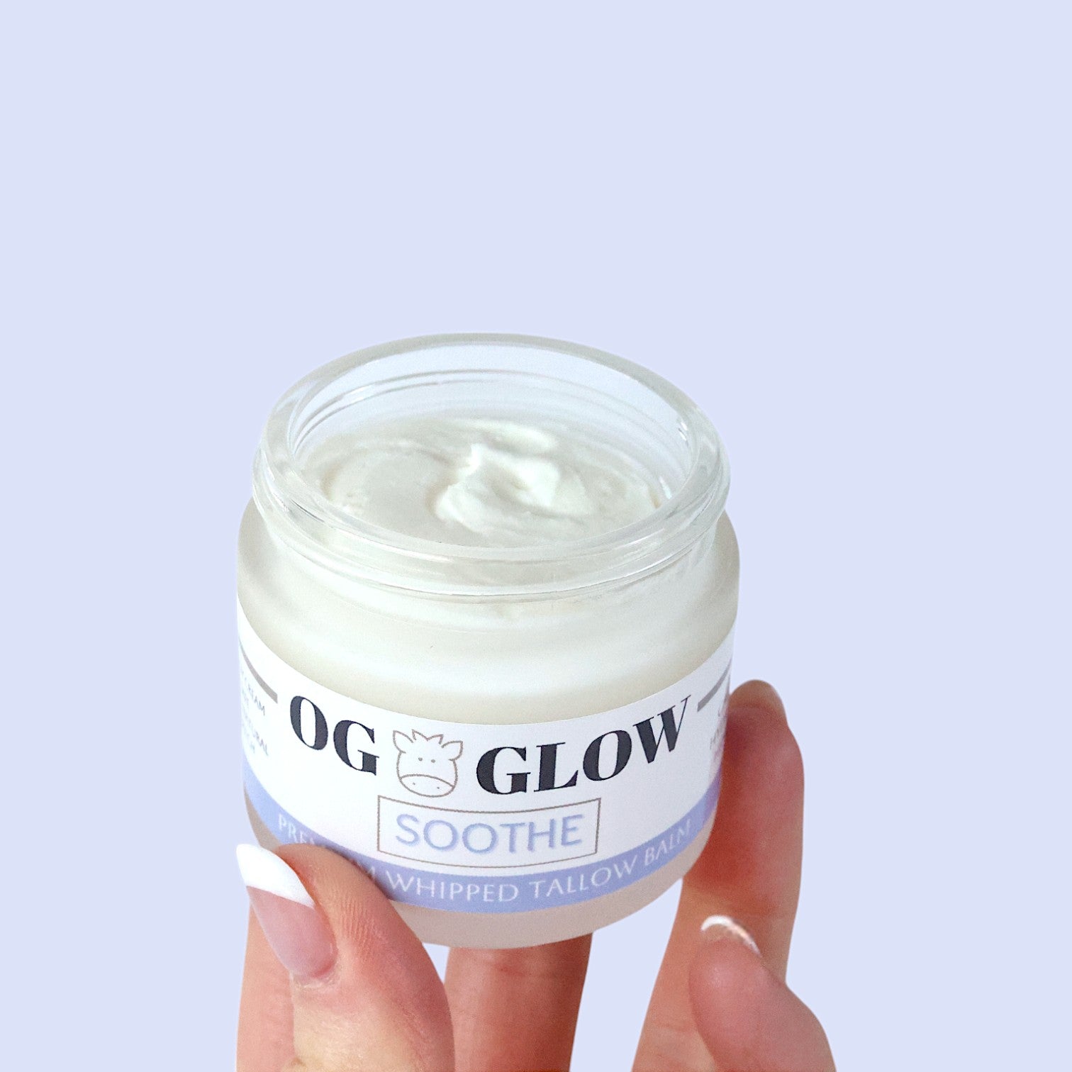 Hand holding glass jar of Soothe whipped tallow balm. there is no lid so you can see the texture of the white whipped tallow inside.